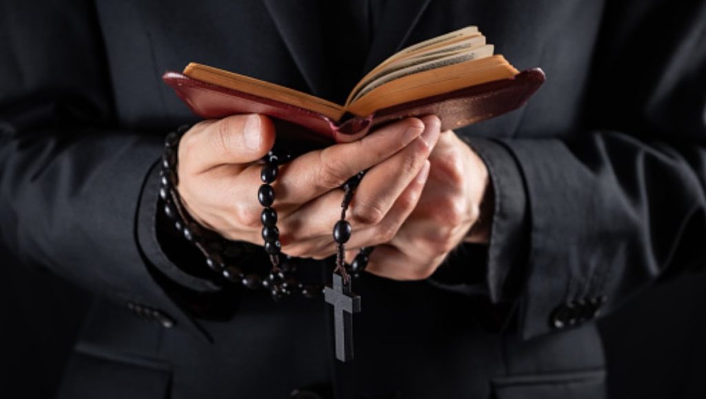 Religious person studies Bible and holds prayer beads, low-key imag