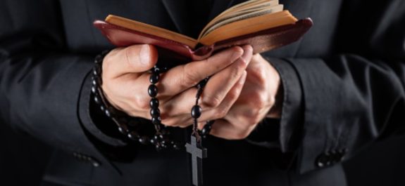 Religious person studies Bible and holds prayer beads, low-key imag