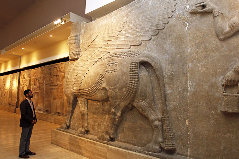 A man looks at ancient Assyrian human-headed winged bull statues at the Iraqi National Museum in Baghdad